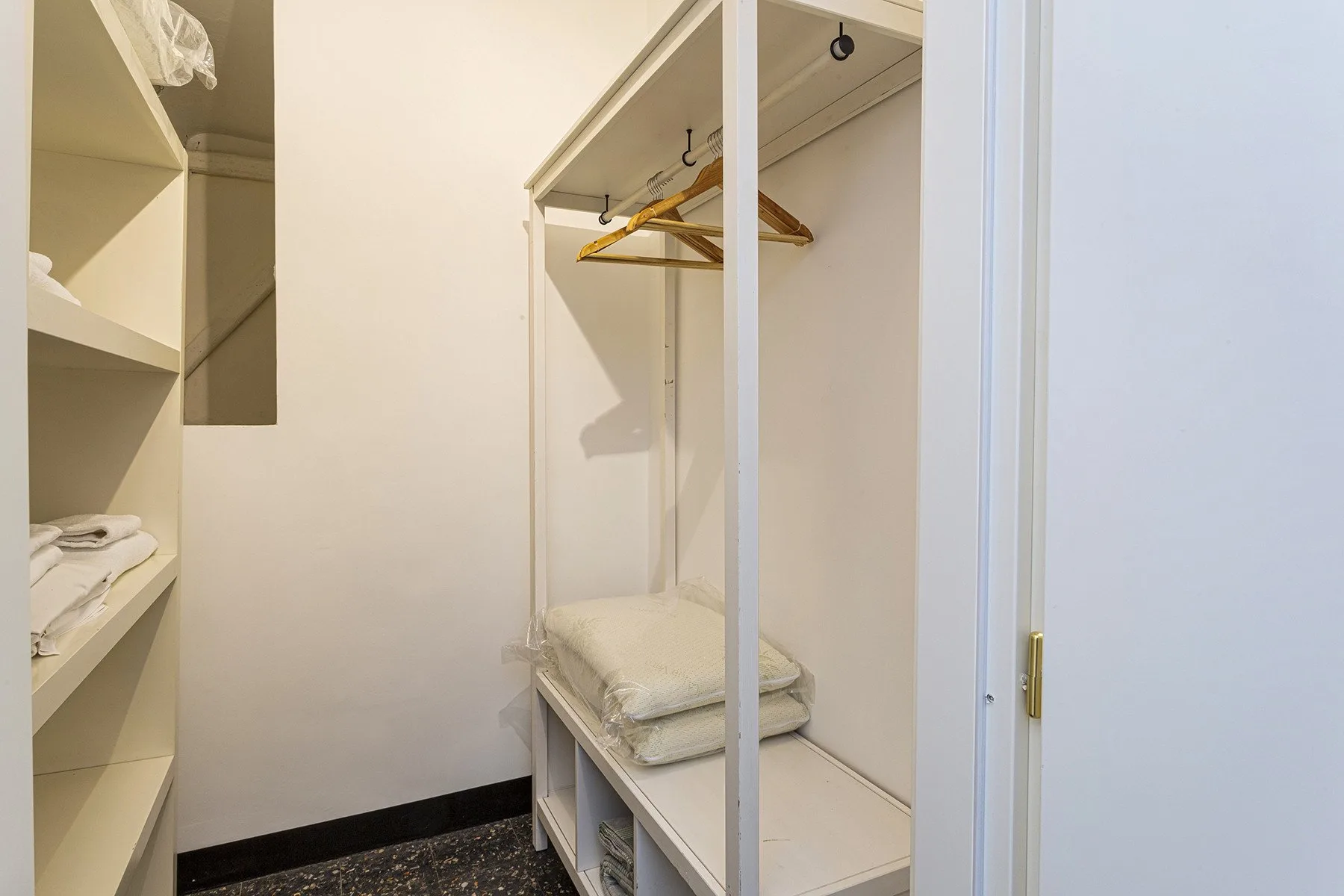 Un vestidor tiene estantes abiertos, espacio para colgar ropa y ropa de cama doblada.