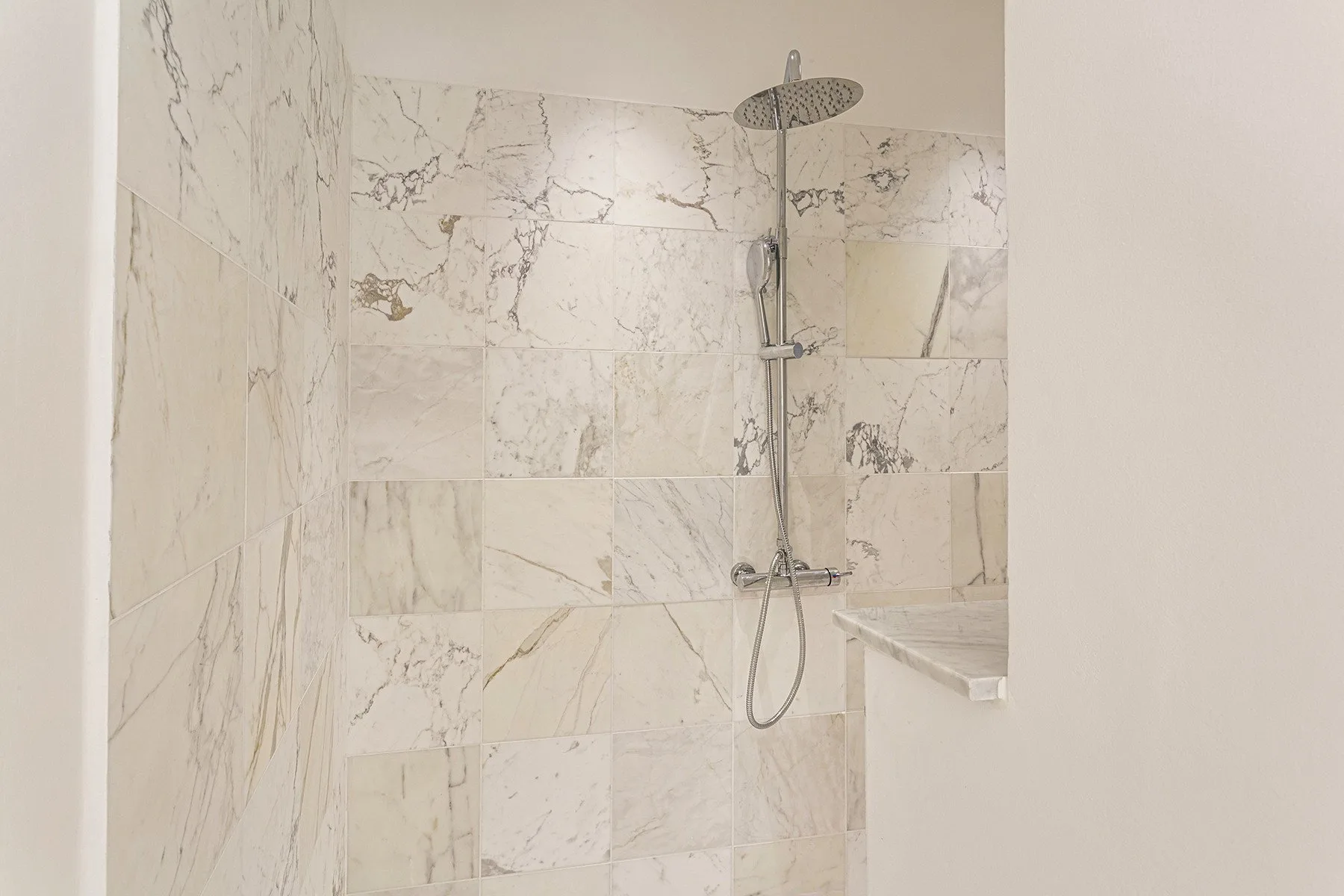 Una zona de ducha con azulejos, rociador fijo y ducha de mano.