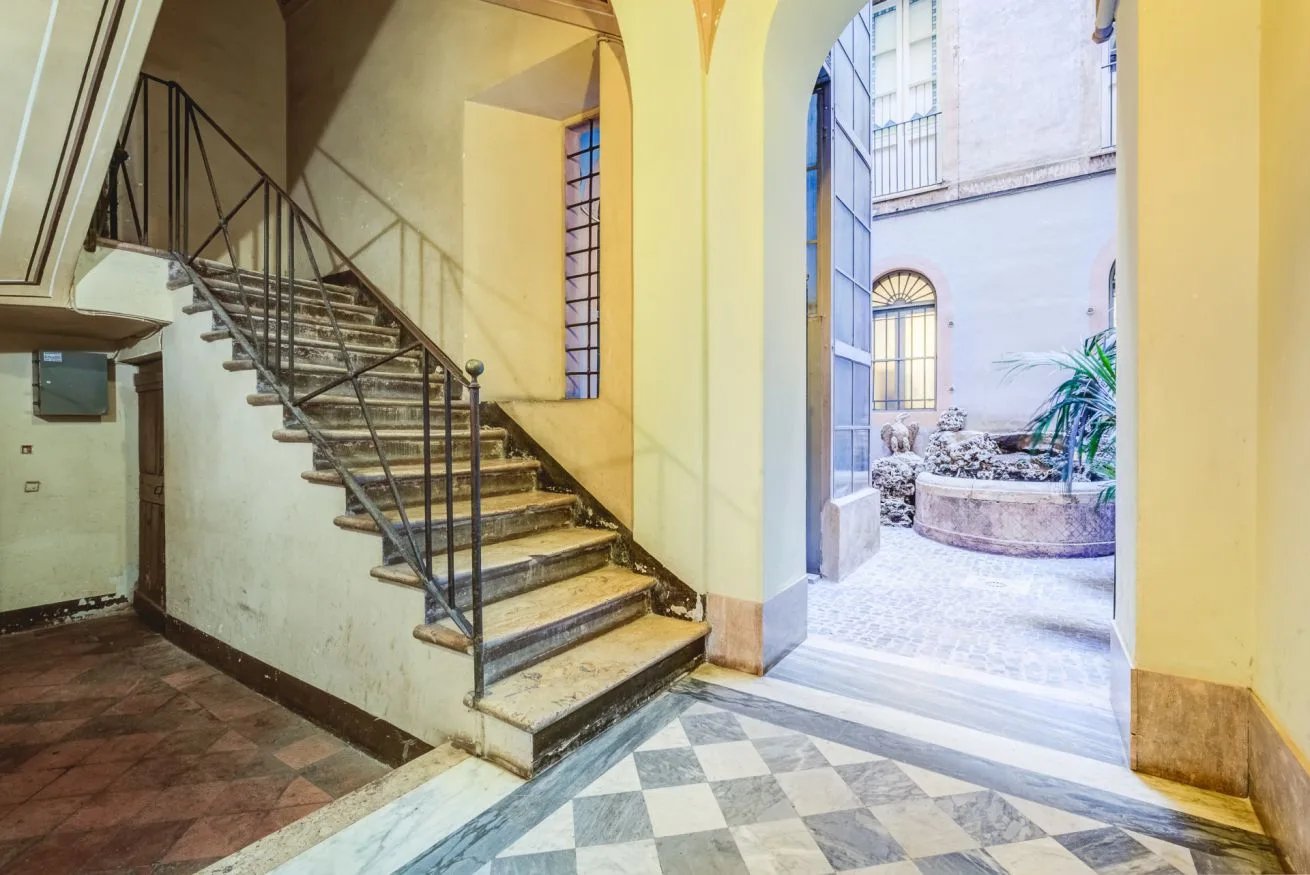 An indoor entry hall with a staircase beside an arched opening to a courtyard.