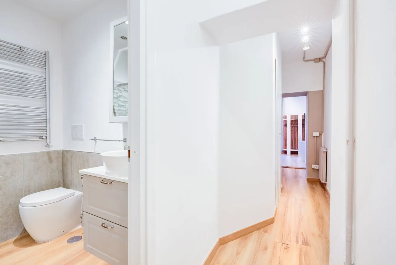 A bright bathroom opens onto a hallway with wood flooring.