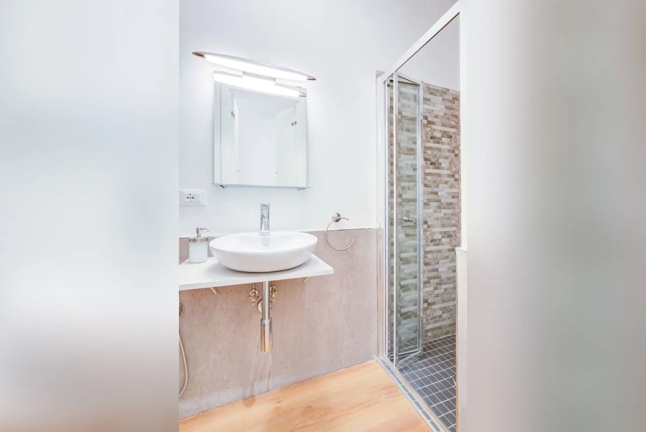 A bright bathroom with a sink, mirror, and glass shower.