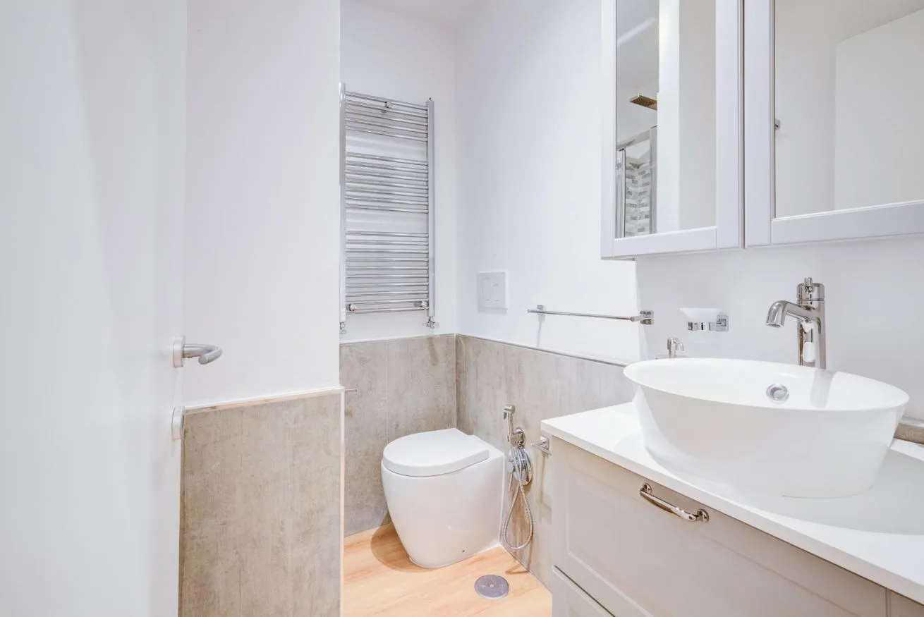 A bright bathroom with a sink, toilet, and wall-mounted towel warmer.