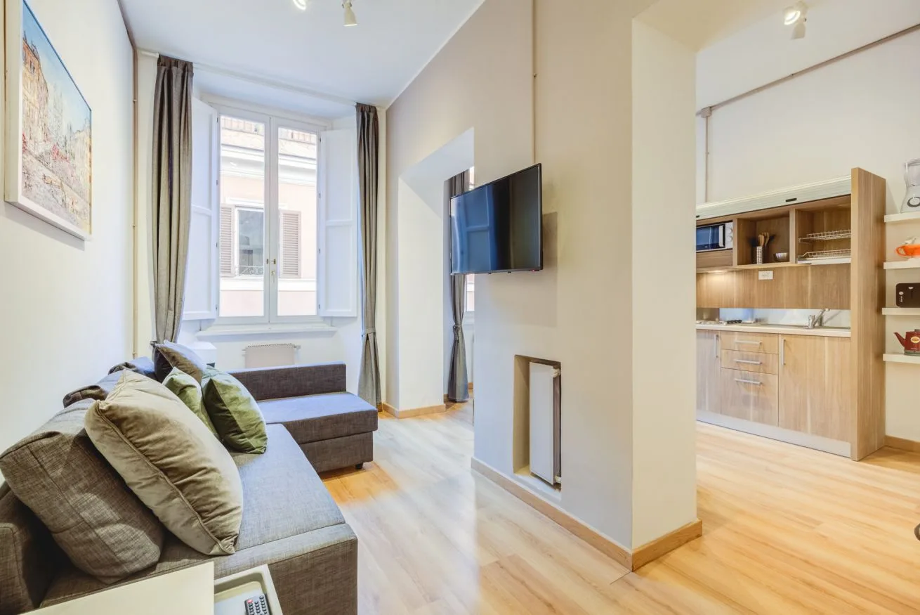 A living room with seating, a television, and a window beside an open kitchen.