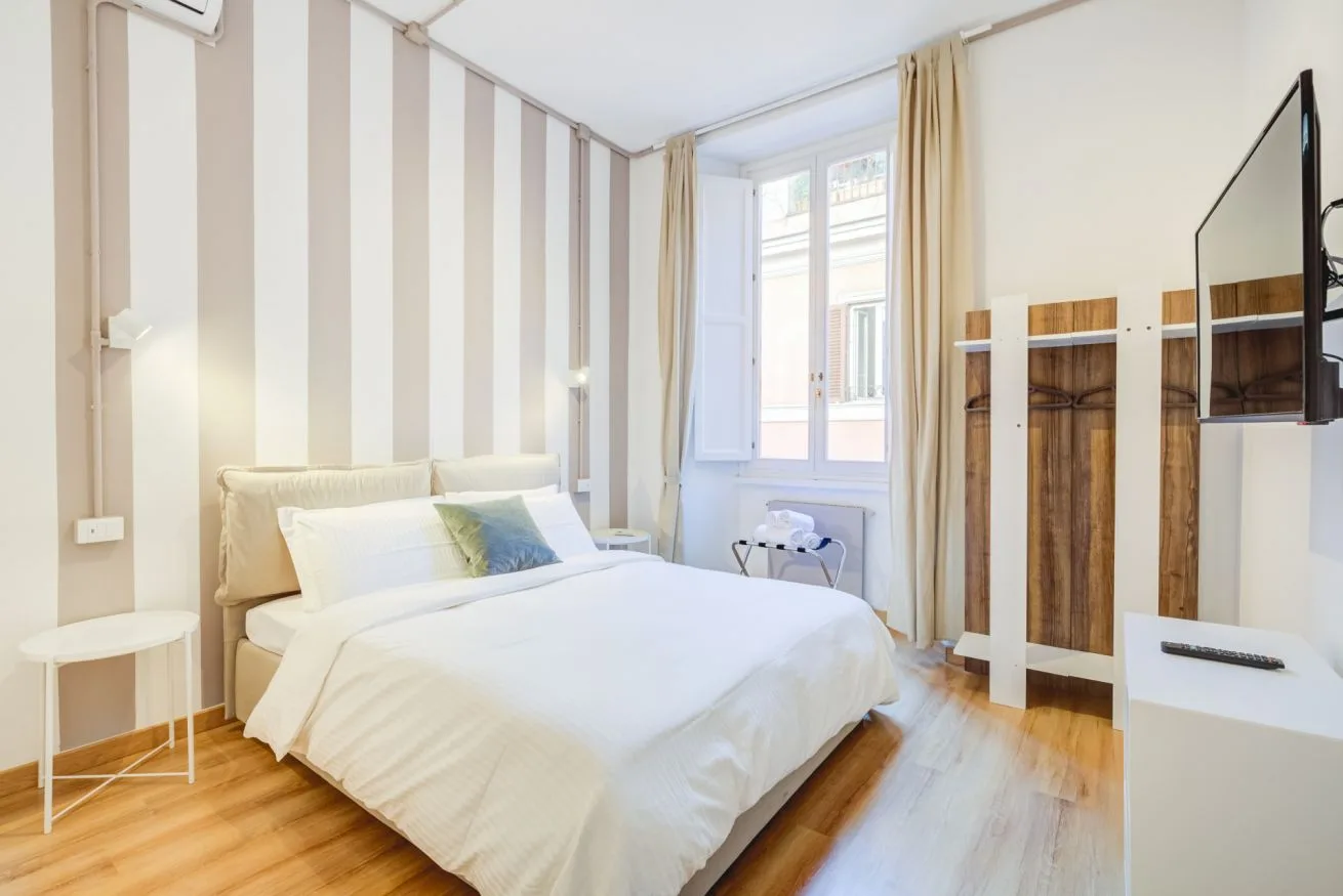 A bright bedroom with a bed beside a window and wall-mounted television.