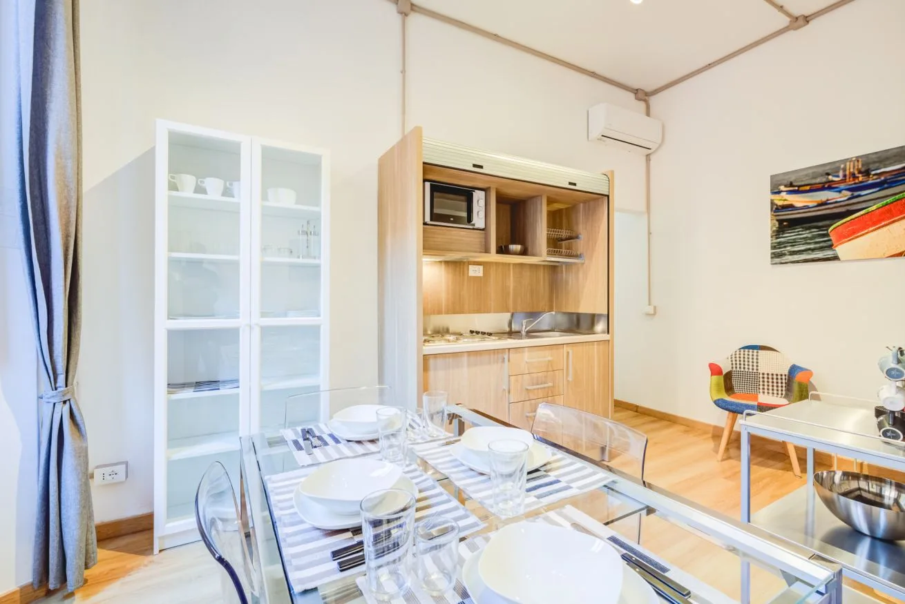 A dining area with a set table beside light wood kitchen cabinets.