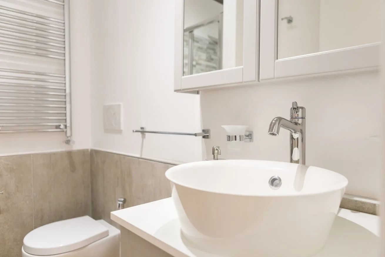 A bright bathroom with a white vessel sink and wall-mounted mirror cabinets.