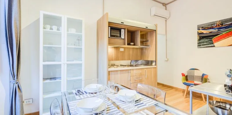 A dining area with a set table, glass-front cabinet, and compact kitchenette.