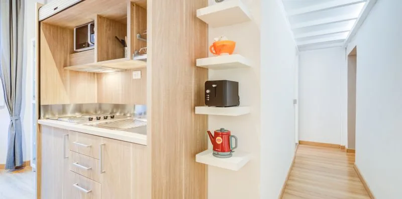Una cocina compacta da a un pasillo luminoso con suelo de madera clara.