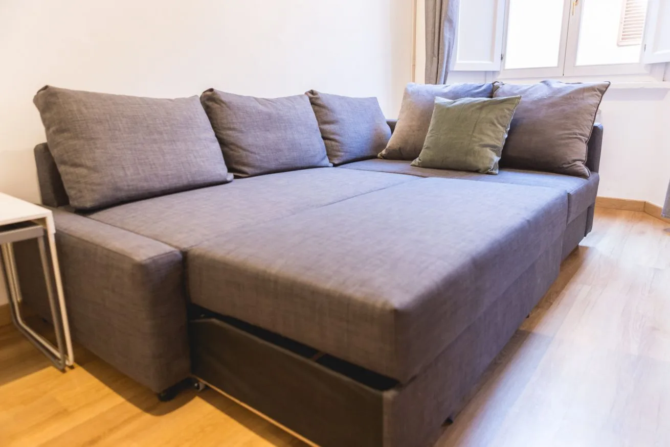 A gray sectional seating area sits beside a window in a bright room.