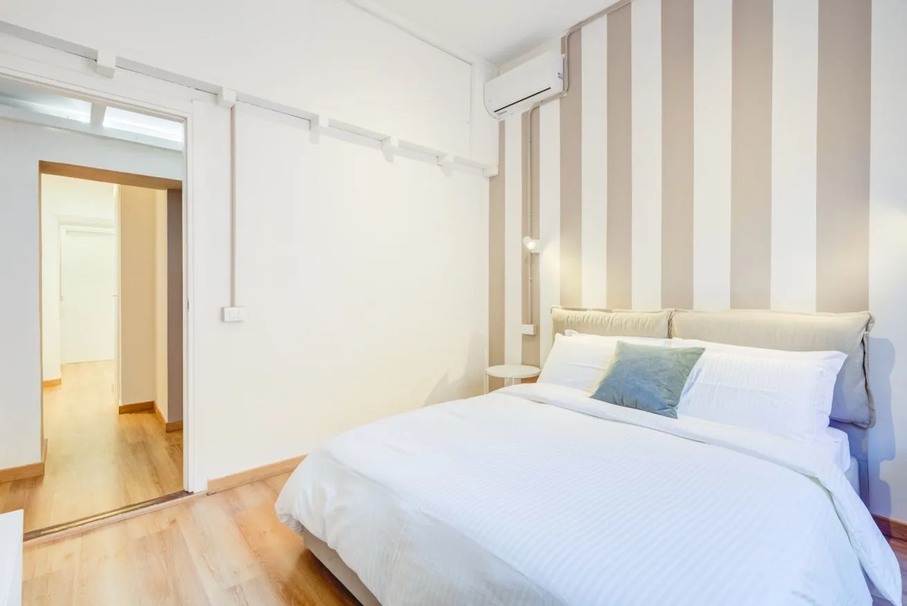 A bedroom with a large bed against a wall with vertical stripes.