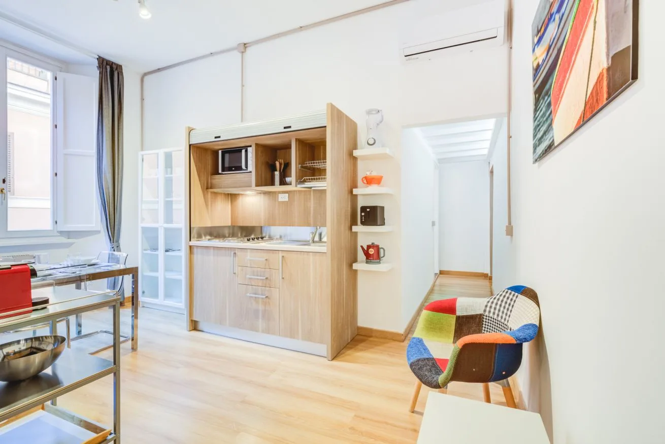 A bright kitchenette and dining area with wood cabinetry and colorful seating.