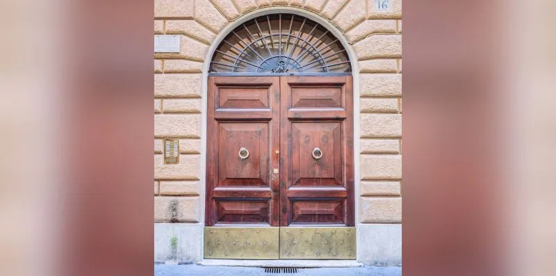 A wooden double door with an arched window set in a stone facade.