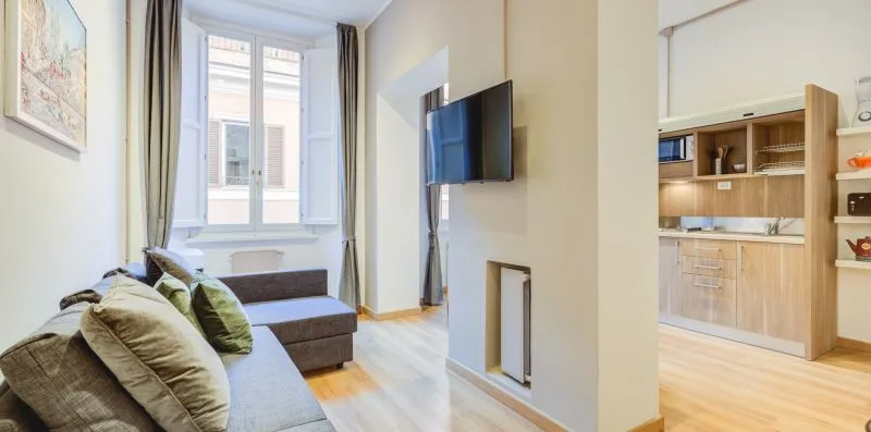 A bright living area with seating, a wall-mounted television, and a kitchenette.