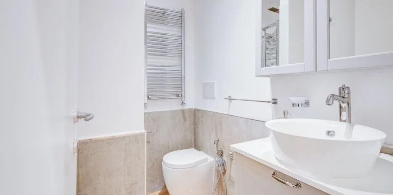 A bathroom with a toilet, a vessel sink, and a wall-mounted towel warmer.
