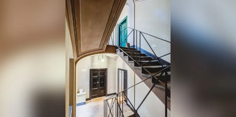Interior staircase with dark steps and metal railings beside a tall window.