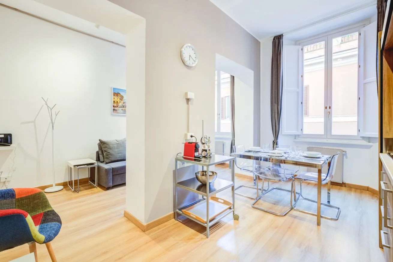 A bright dining area with a glass table and seating beside tall windows.