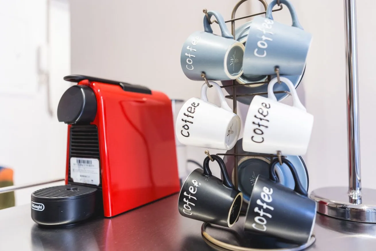 A red coffee machine sits beside a rack of hanging mugs on a counter.