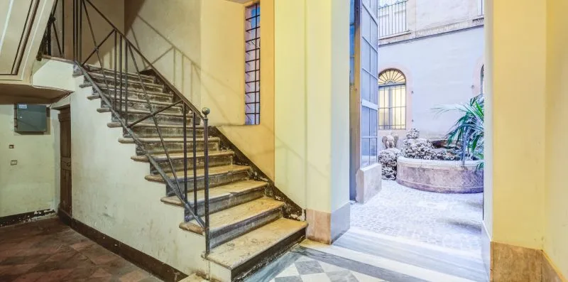 An interior stairway opens onto a bright courtyard with a circular planter.