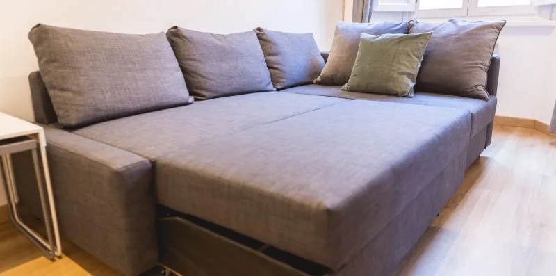 A gray sectional seating area with cushions sits beside a window.