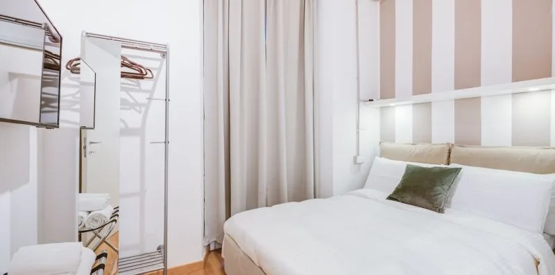 A bedroom with a white bed, striped walls, and a clothing rack.