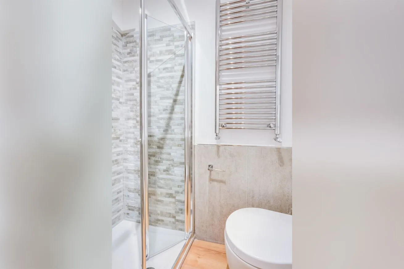 A bathroom with a glass shower, tiled walls, and a towel radiator.