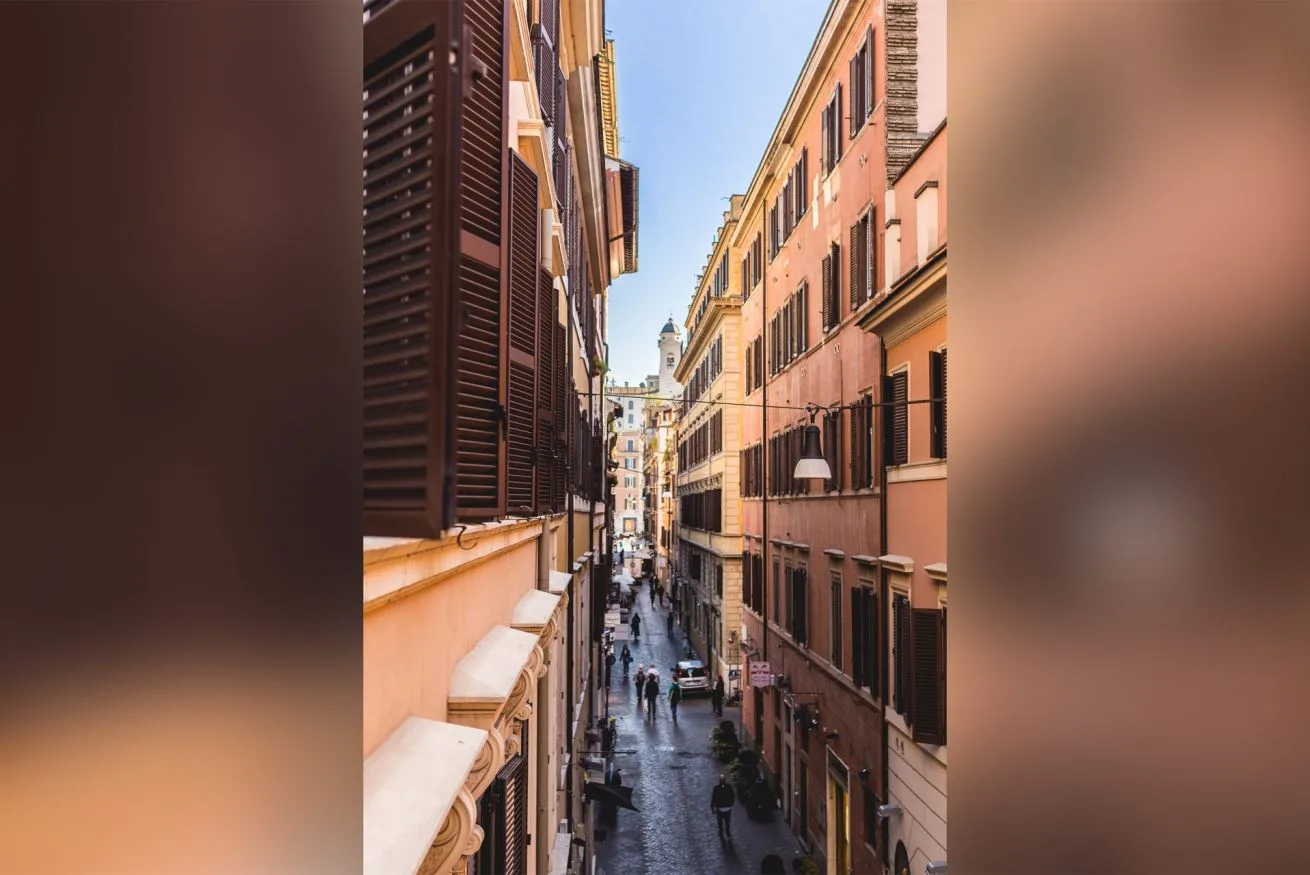 A narrow city street runs between tall buildings, with pedestrians below.