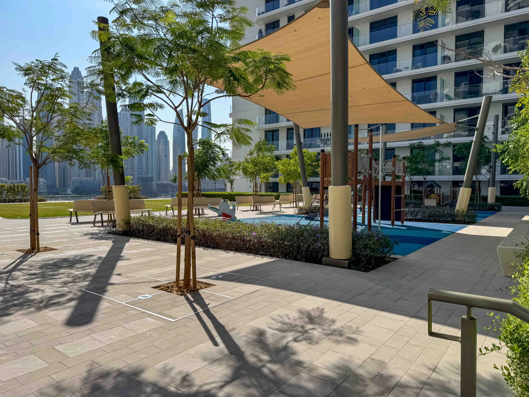 Zona de piscina al aire libre con asientos a la sombra junto a un edificio moderno.
