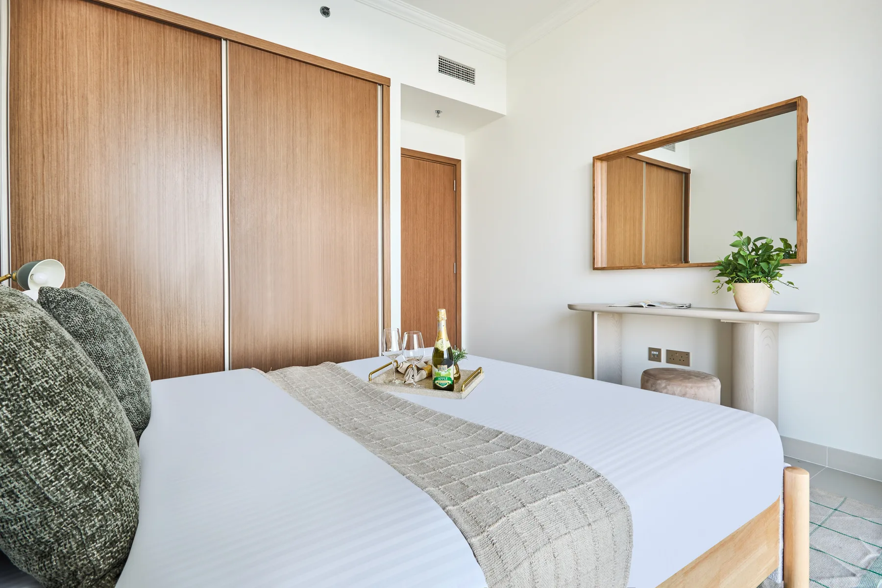 Un dormitorio con una cama, armarios de madera y un pequeño escritorio bajo un espejo.