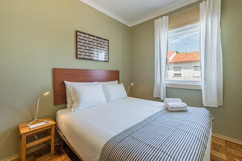 Un dormitorio con una cama bien tendida y una ventana enmarcada por cortinas blancas.