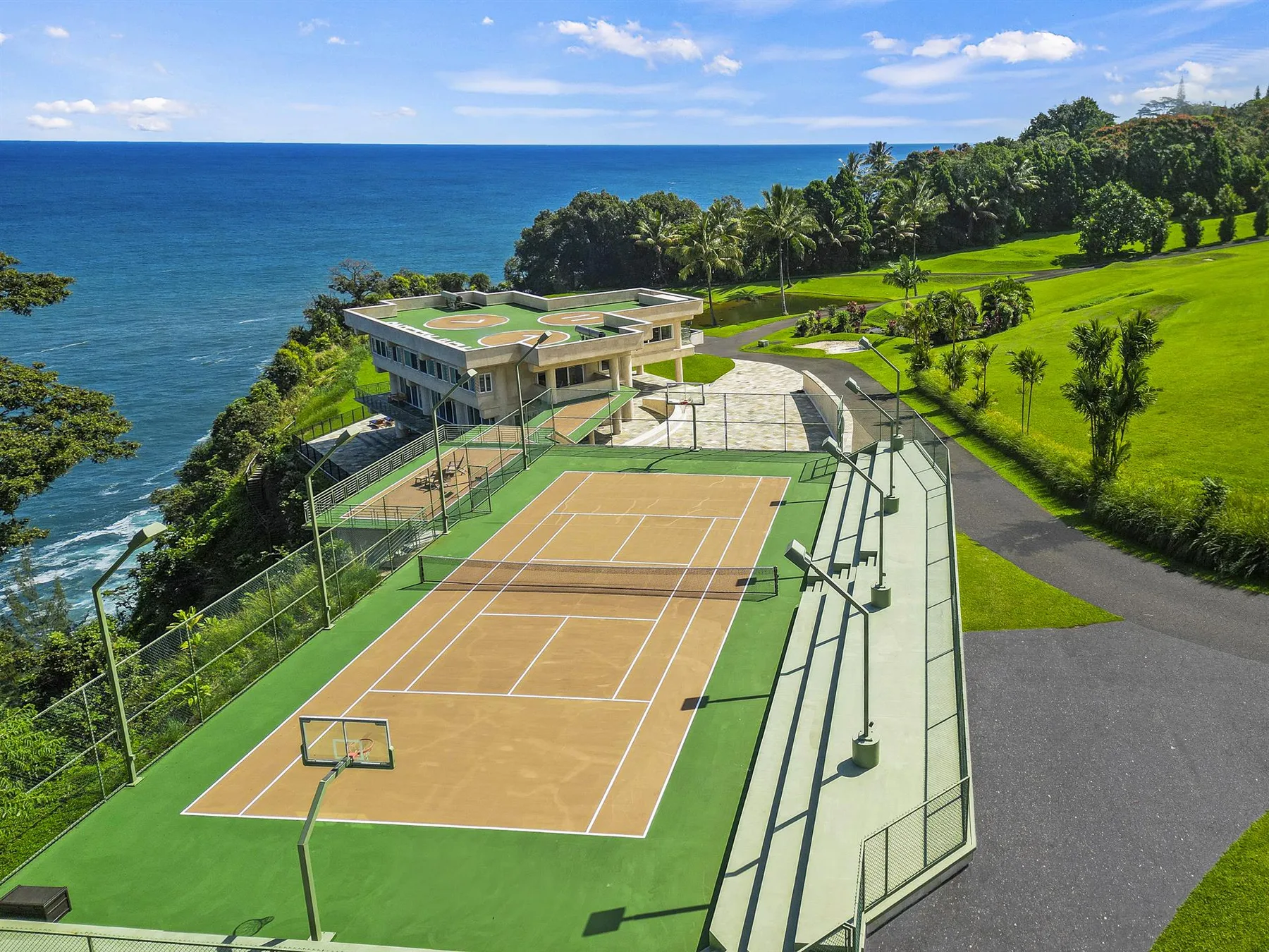 An outdoor sports court beside the ocean, with green grounds and trees.
