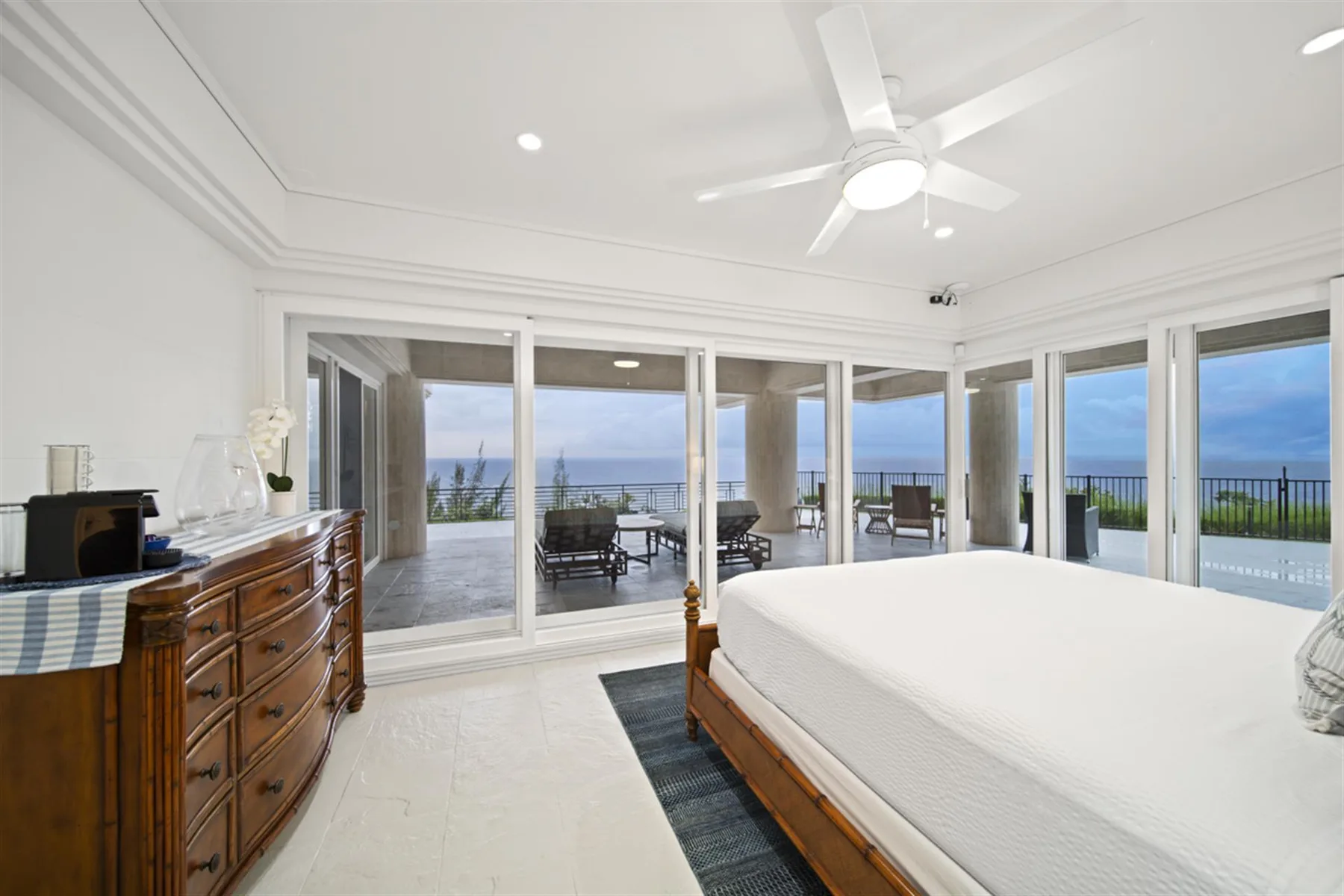 A bright bedroom with a bed and broad windows overlooking a balcony.