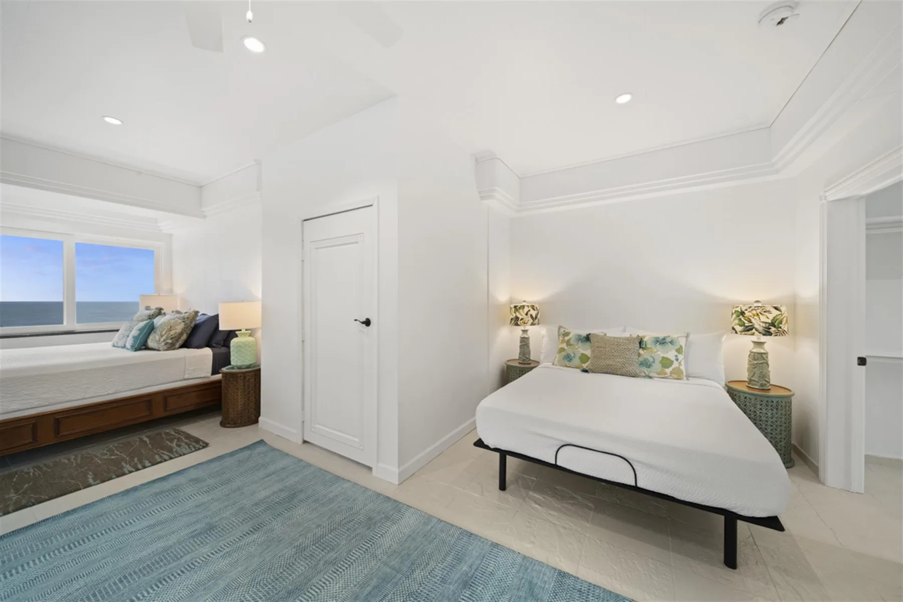 A bright bedroom with two beds and a blue rug.