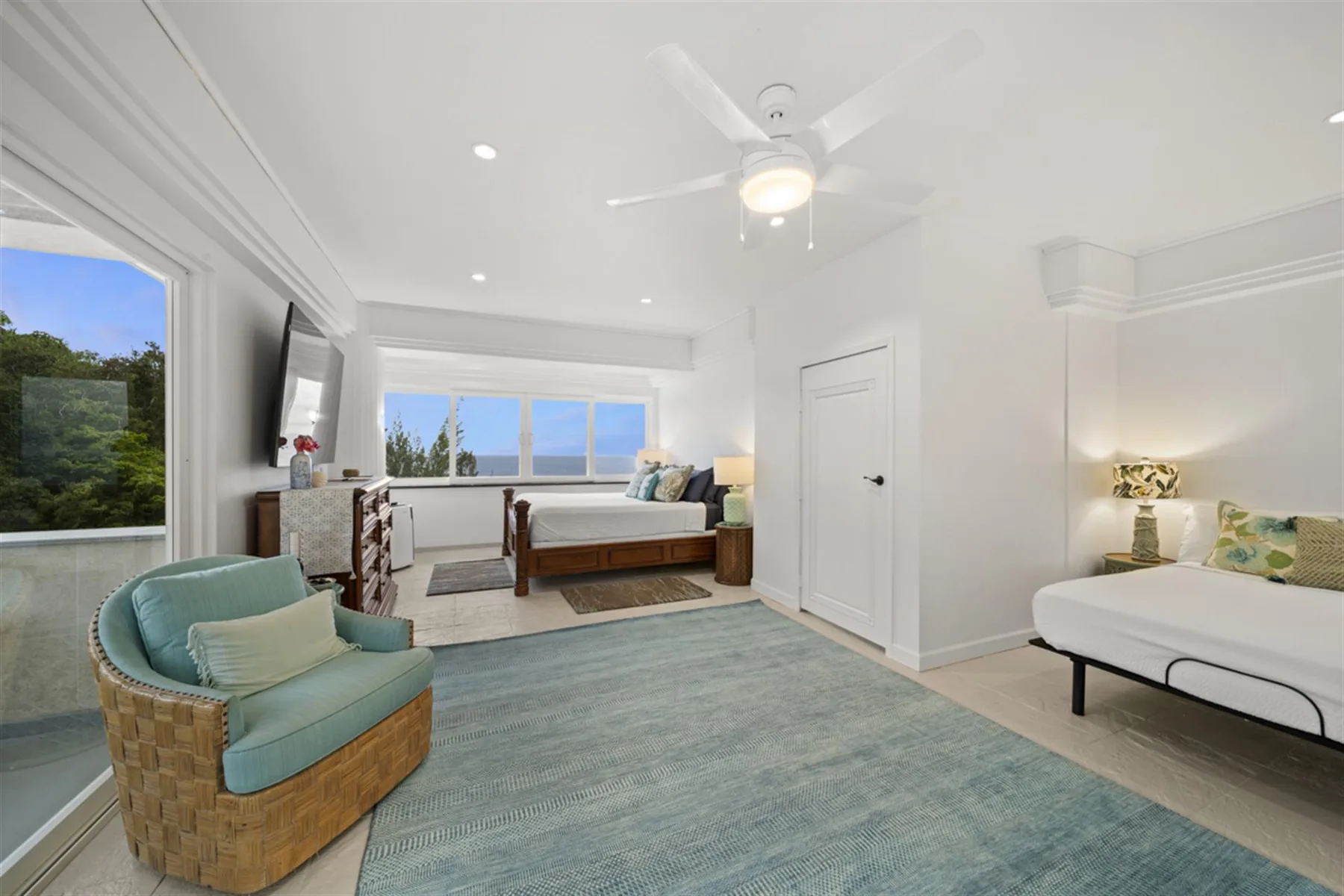A bright bedroom with beds, a ceiling fan, and a blue rug.