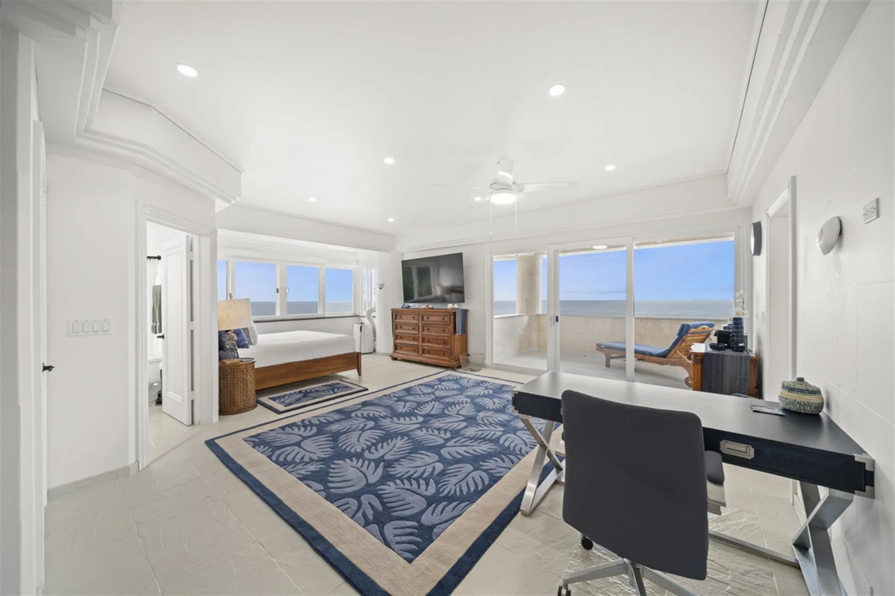 A bright living room with a patterned rug, seating, and large windows overlooking the water.