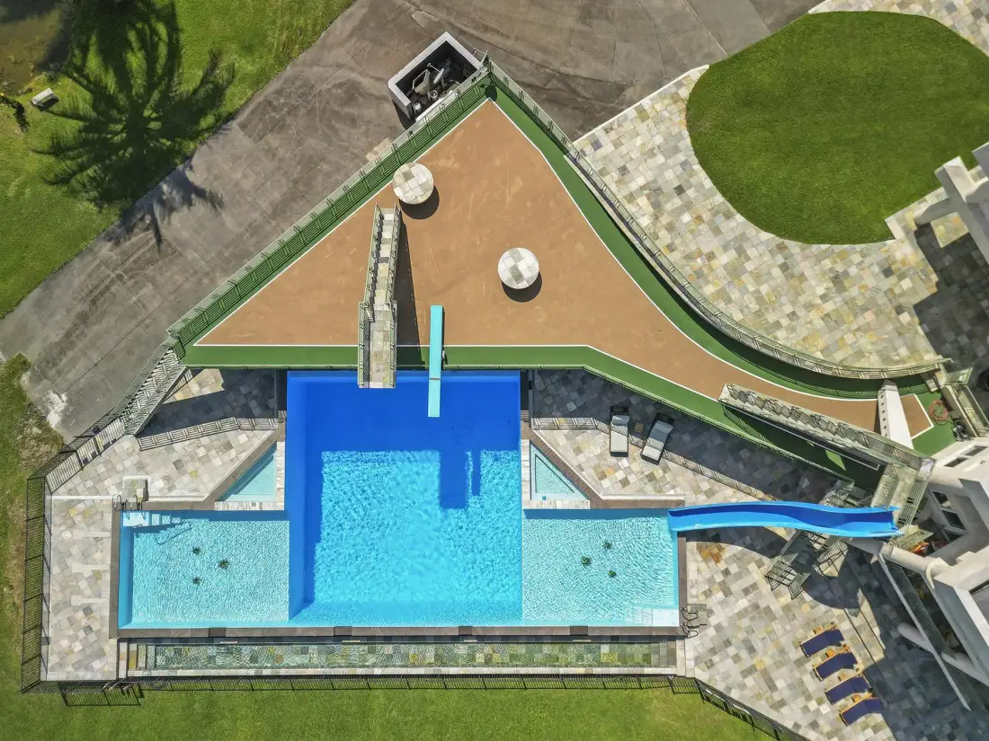 An aerial view of an outdoor pool beside a paved patio and lawn.