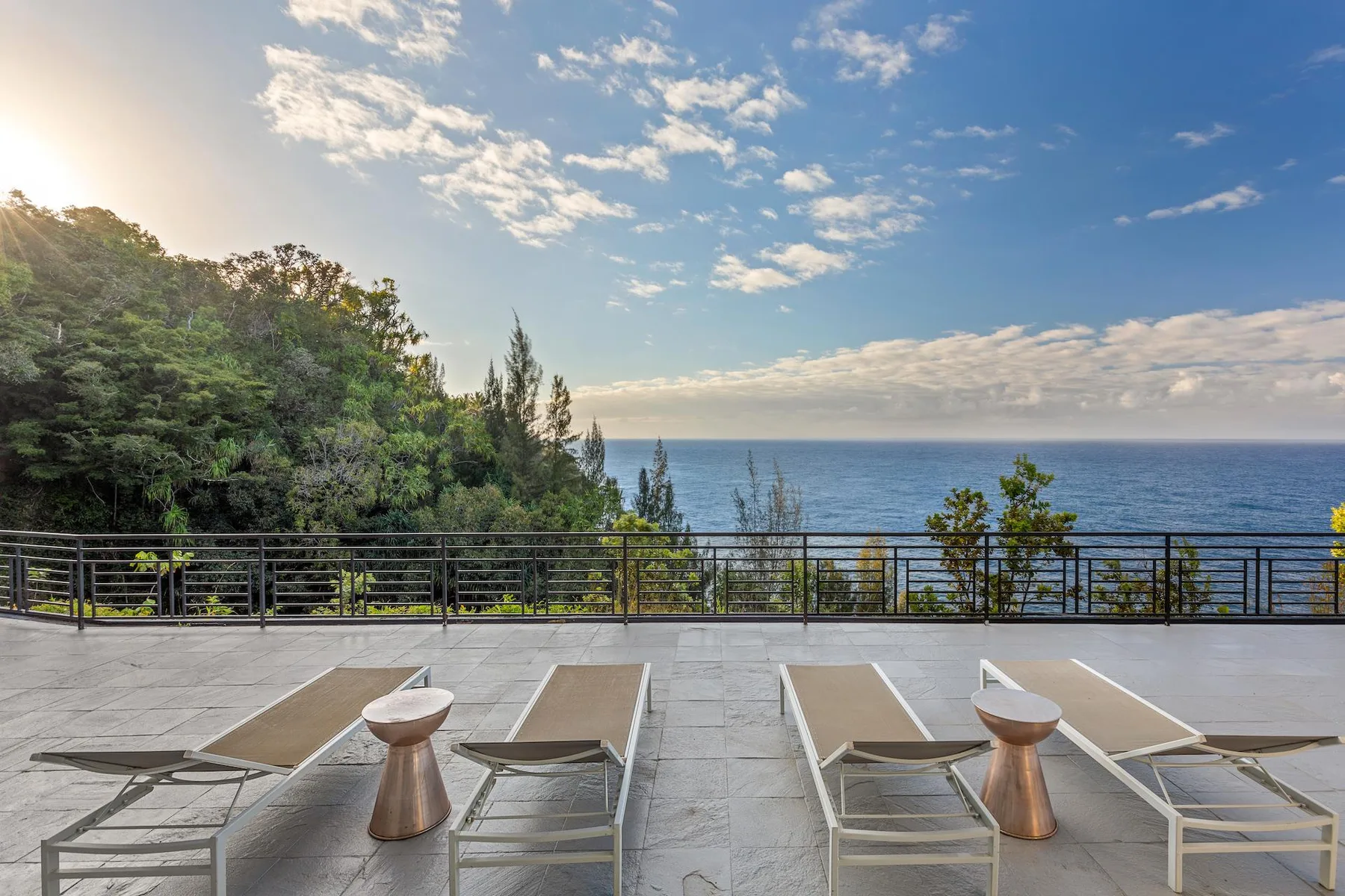An outdoor terrace overlooks the ocean, with lounge seating and a railing.
