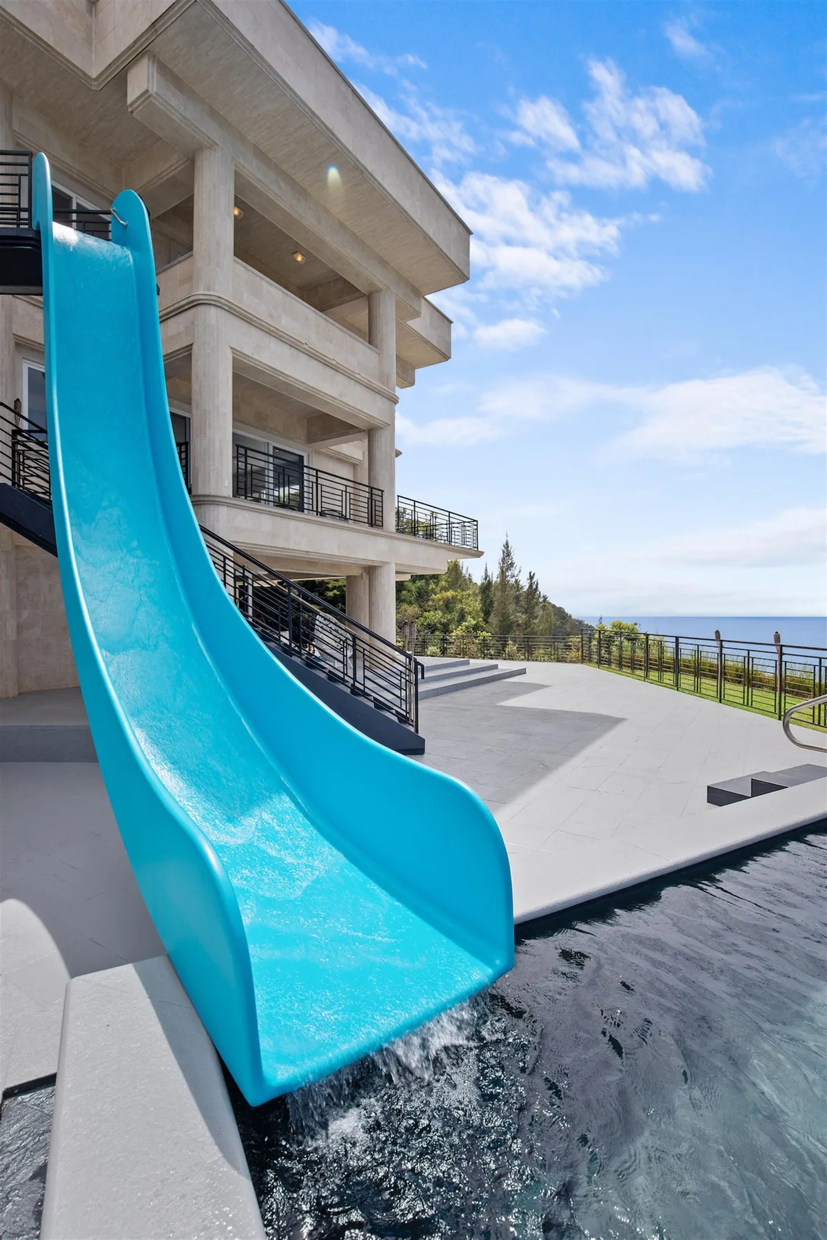 An outdoor pool with a tall blue slide beside a modern building.