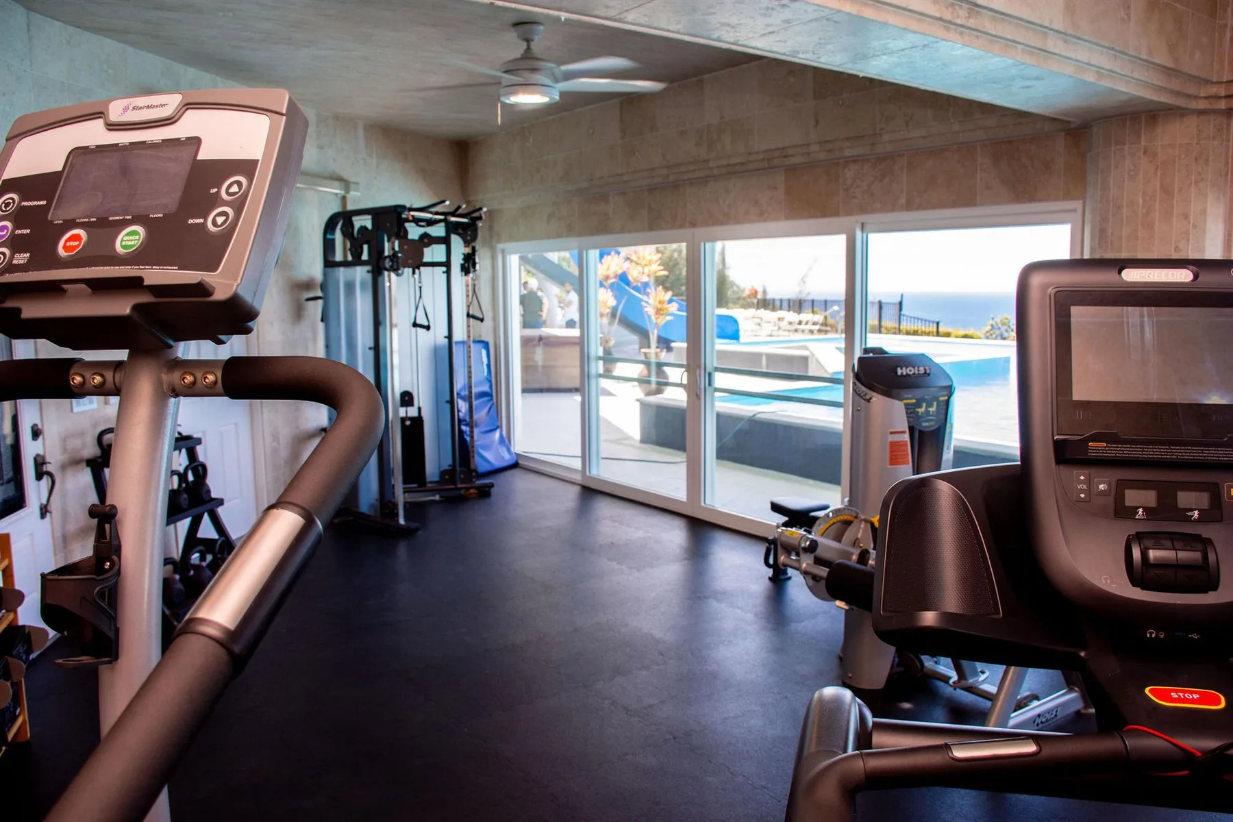A gym with exercise equipment and large windows overlooking an outdoor pool.