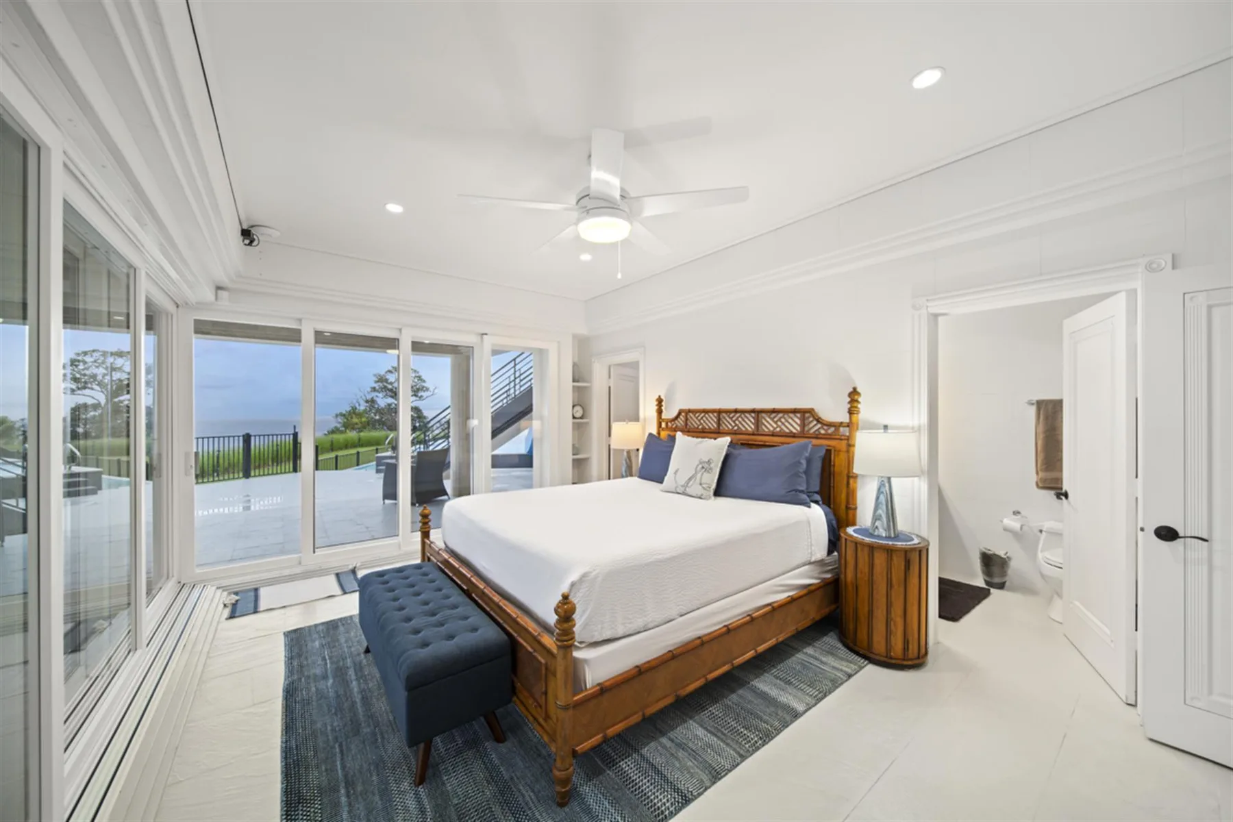 A bright bedroom with a wooden bed, blue seating, and glass doors opening to a patio.