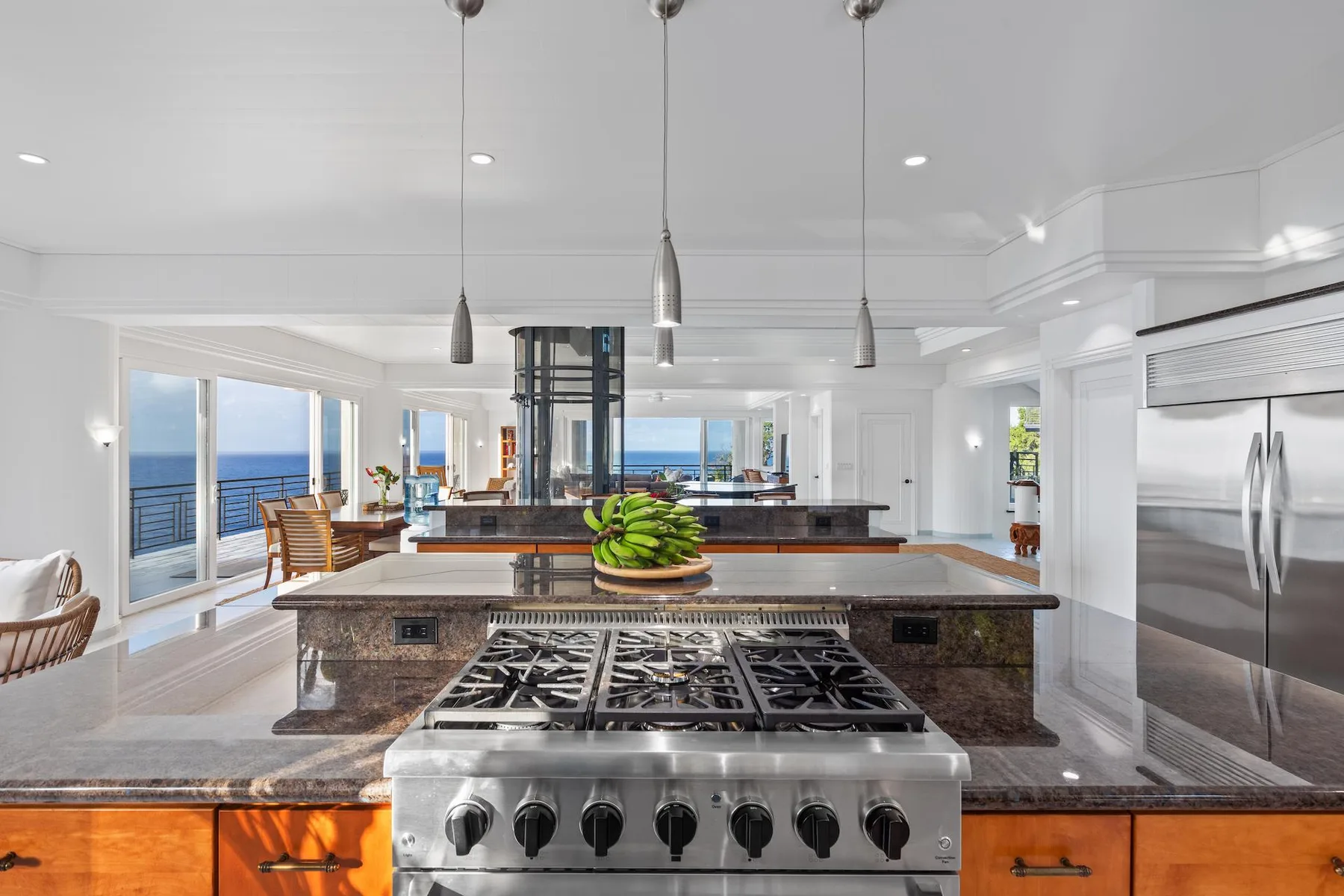 A bright kitchen features a large island with a cooktop and ocean views through the windows.