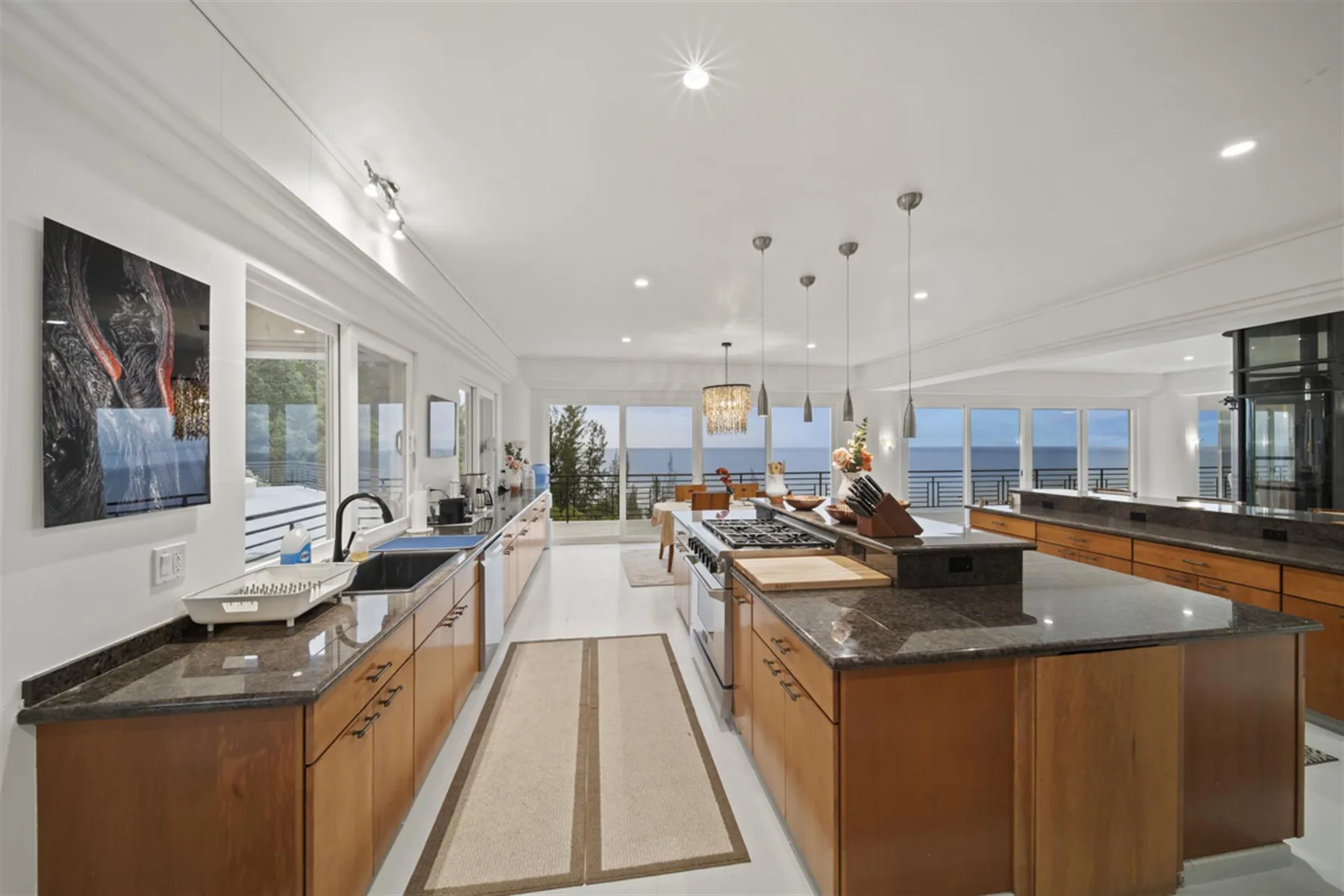 A bright kitchen with wooden cabinetry, a central island, and wide windows overlooking the water.