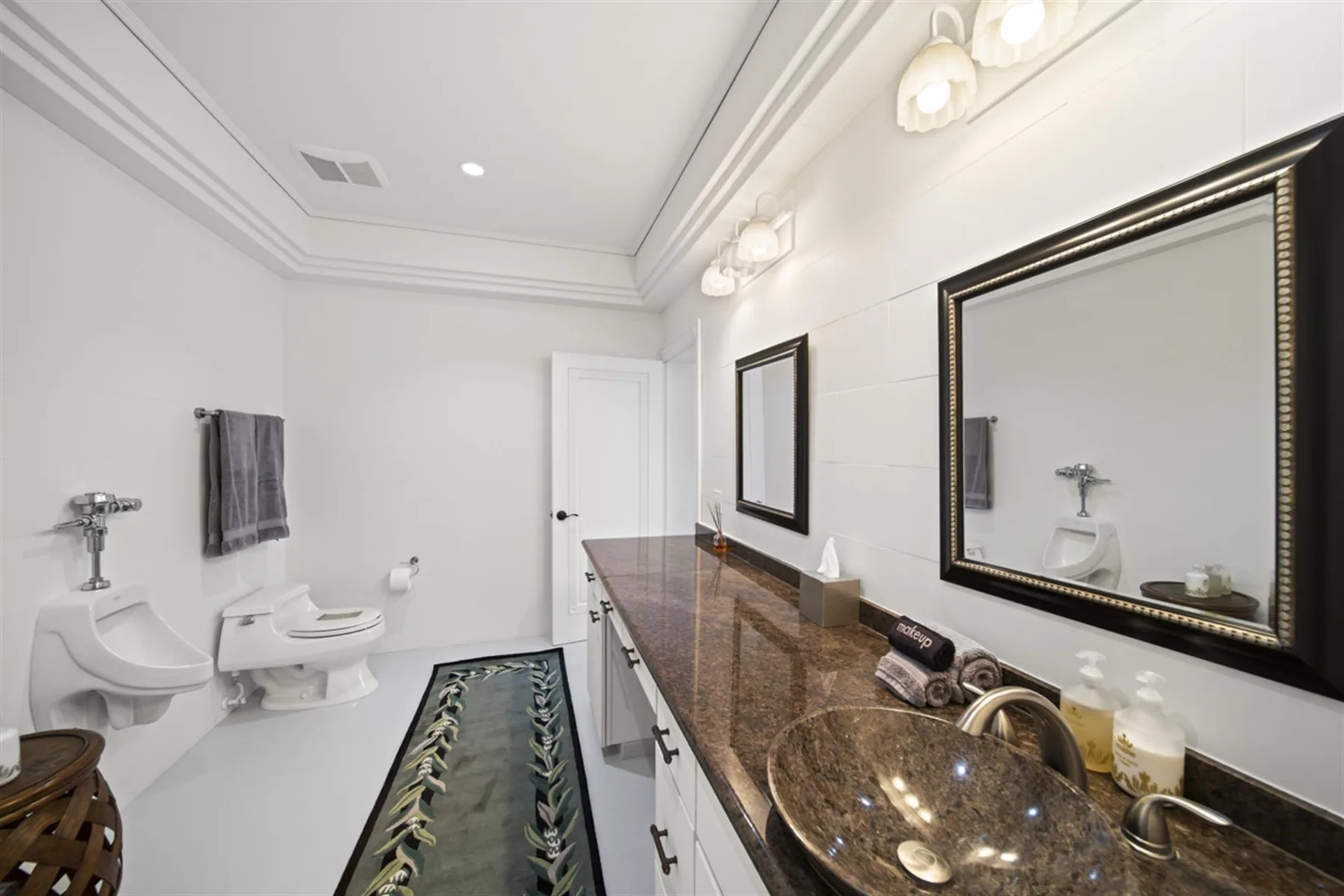 A bright bathroom with a long vanity, large mirrors, and a decorative floor runner.