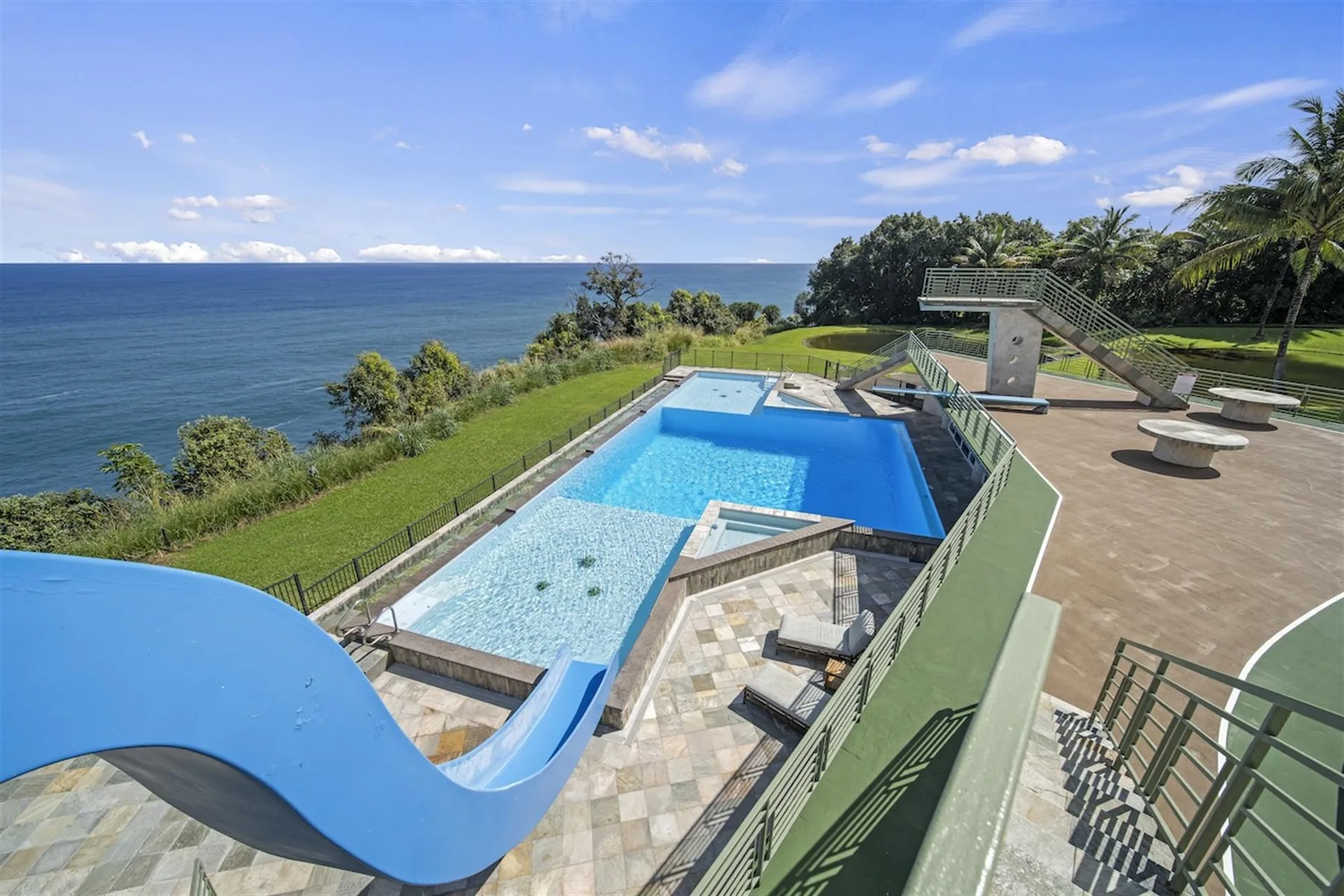 An outdoor pool area overlooks the ocean, with a winding blue waterslide.