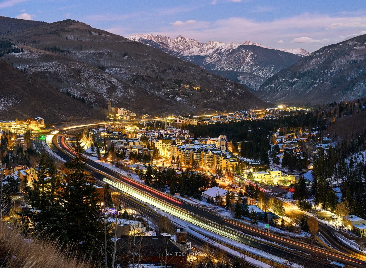 Un pueblo de montaña al anochecer, con carreteras iluminadas que serpentean por el valle.