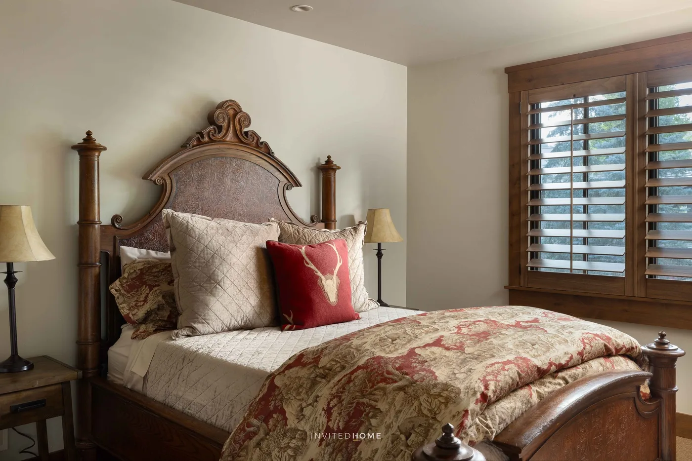 Un dormitorio con una cama de madera ornamentada, ropa de cama estampada y una ventana con persianas de madera.