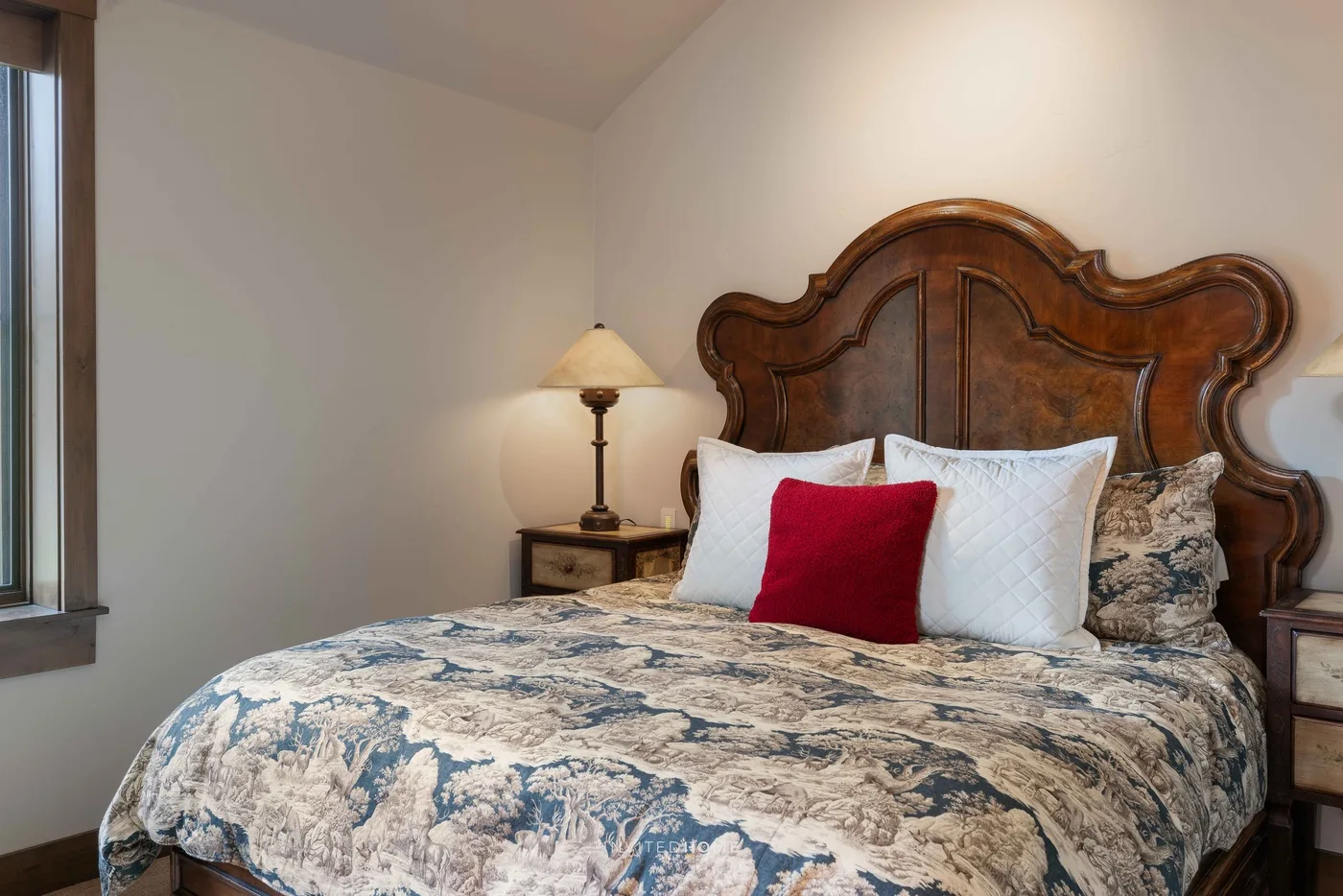 Un dormitorio con una cama cubierta con ropa de cama estampada y un cojín rojo.