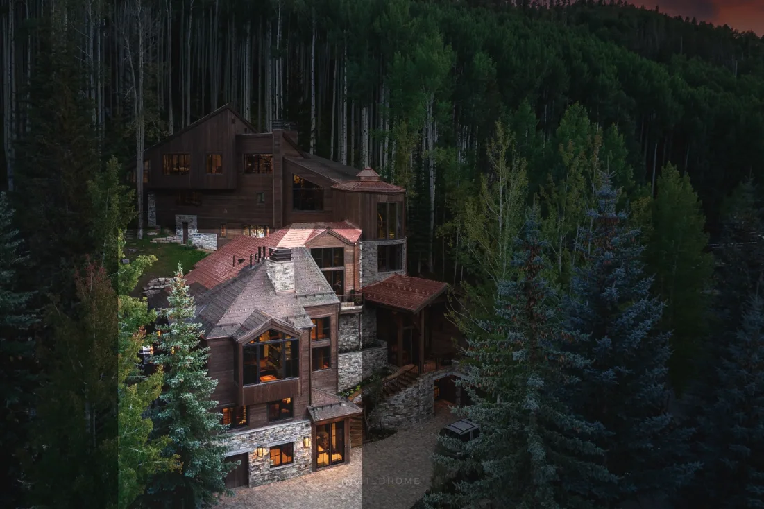 Una casa grande de estilo lodge se encuentra entre densos árboles de hoja perenne.