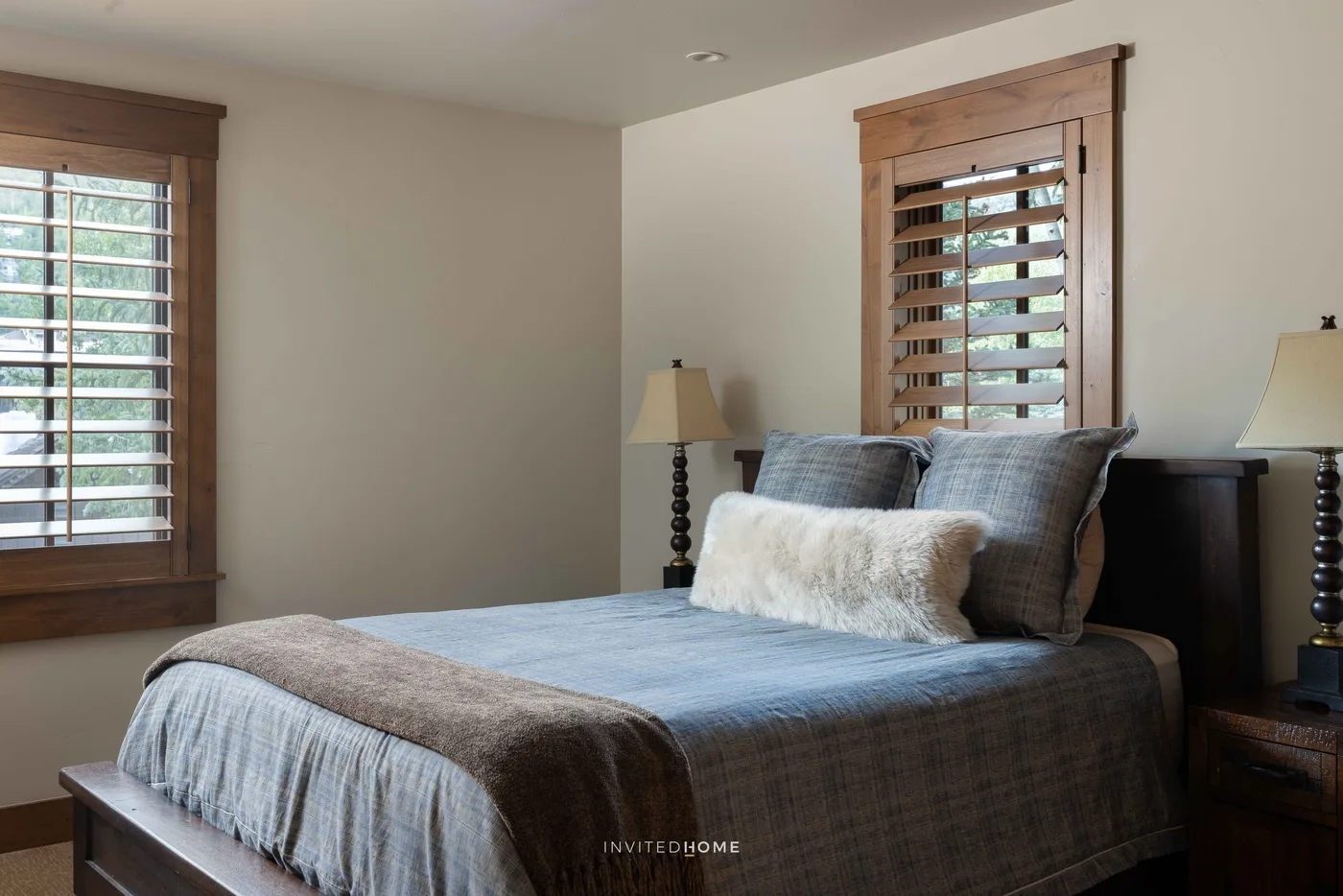 Un dormitorio con una cama vestida con ropa de cama azul y ventanas con persianas de madera.