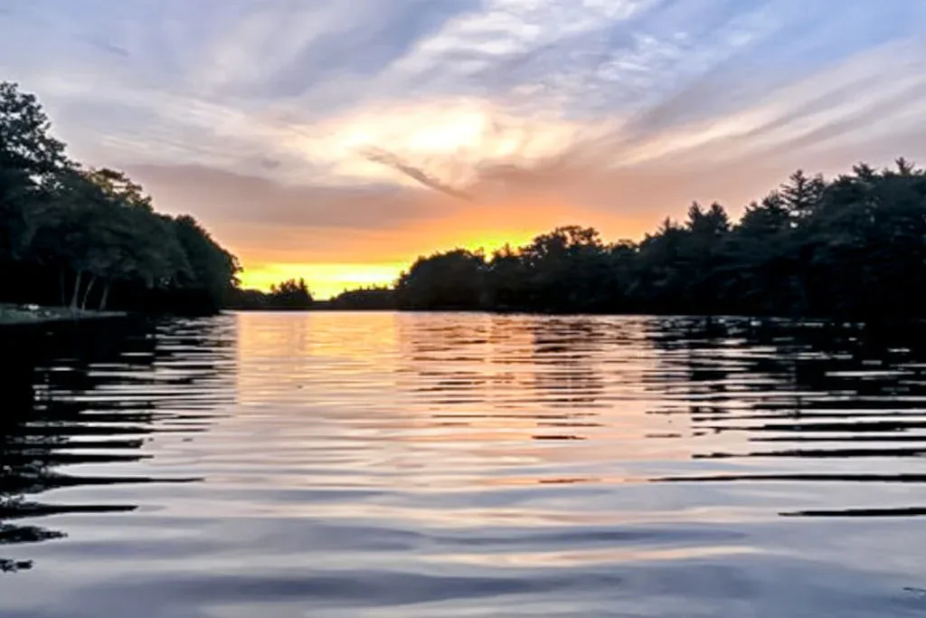A lake reflects a colorful sunset beneath a cloudy sky.