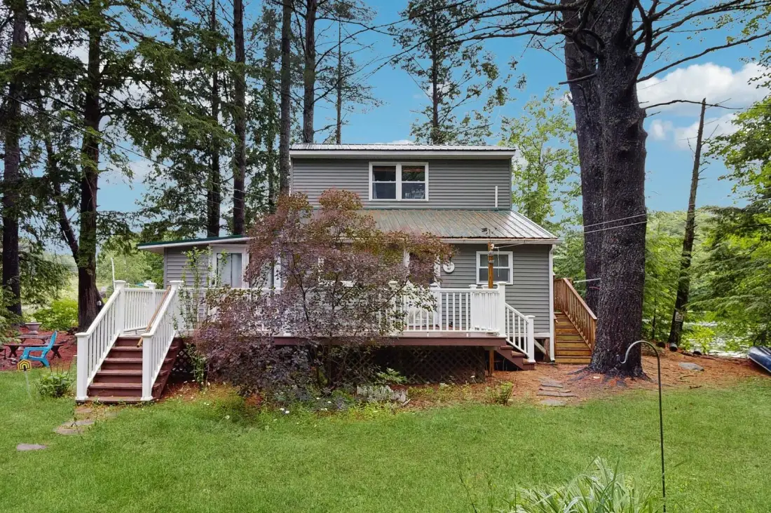 A gray house with a raised wooden deck stands among tall trees.